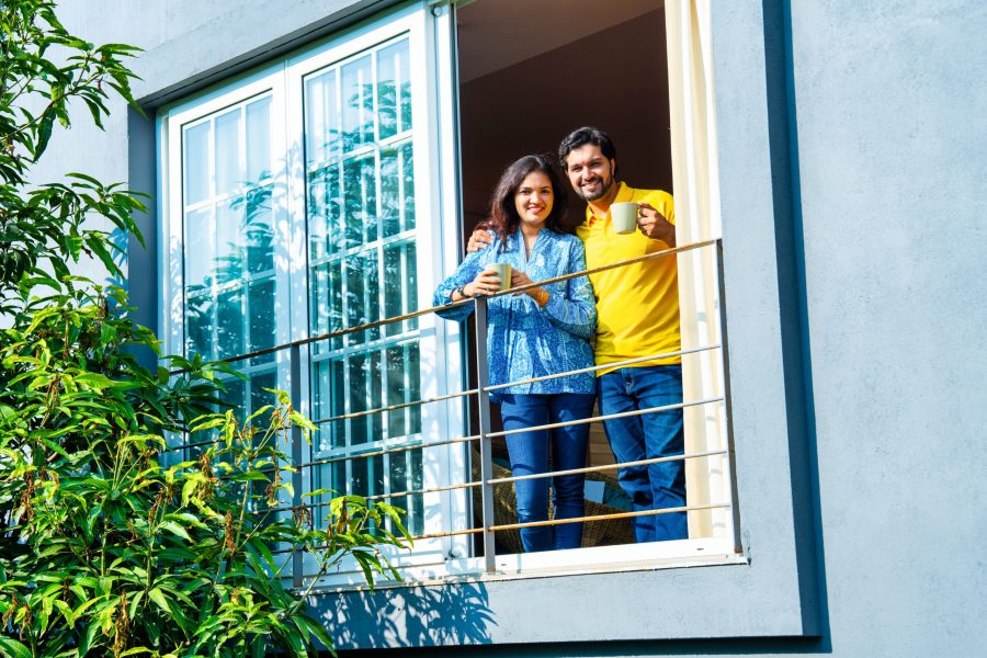 Young Indian couple enjoying morning coffee on balcony, sharing a relaxed conversation in warm sunlight, view from below